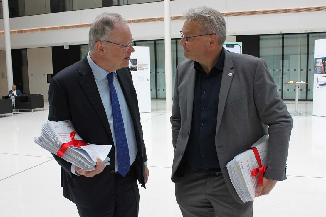 Zwei Männer mit großen Papierstapeln in der Hand reden miteinander. 