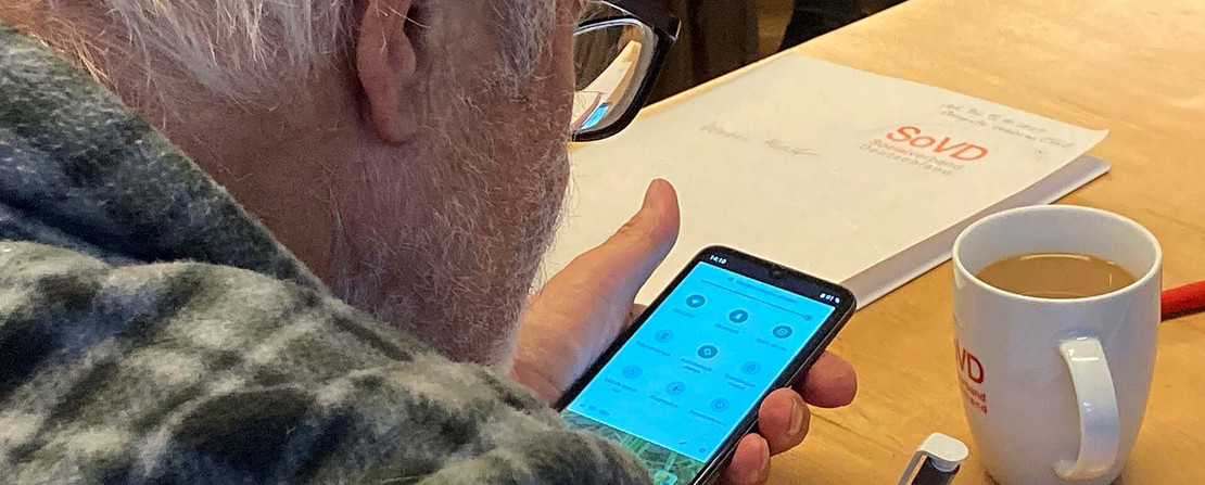 Mann blickt auf ein Handy und macht Notizen, vor ihm SoVD-Material