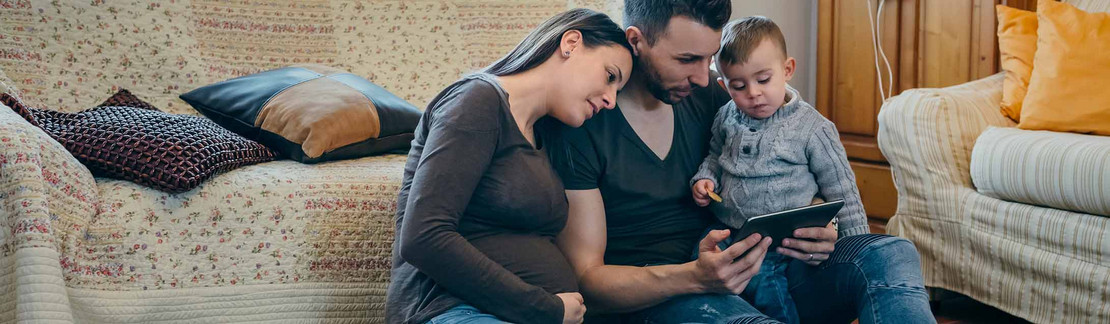 Familie sitzt vor dem Sofa auf dem Boden und schaut in ein Tablet