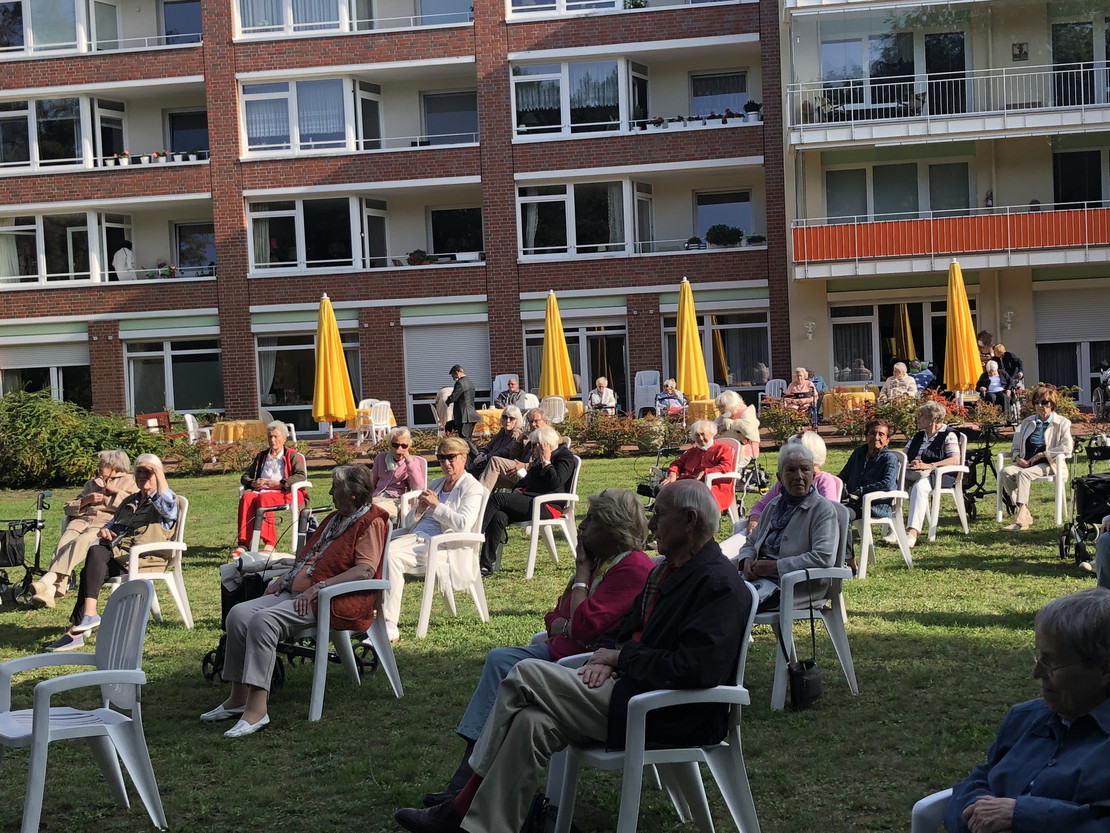 Senioren sitzen im Hof und verfolgen die Musik. 